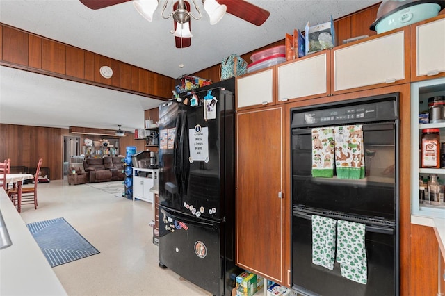 kitchen with a ceiling fan, black appliances, wood walls, concrete floors, and brown cabinetry