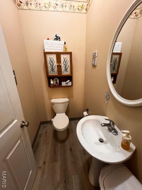 half bathroom featuring wood finished floors, toilet, and a sink