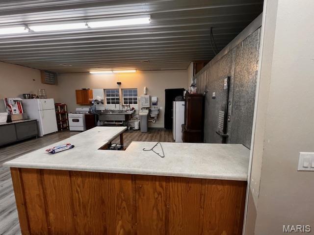kitchen with white appliances, brown cabinetry, wood finished floors, and light countertops