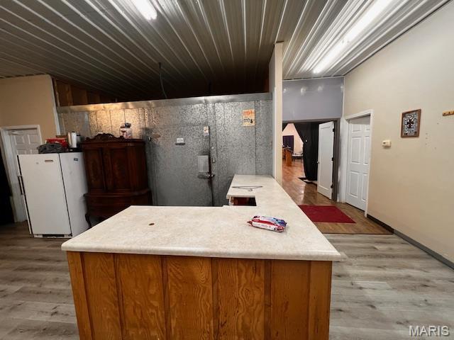 kitchen featuring freestanding refrigerator, light wood-style floors, light countertops, and brown cabinets