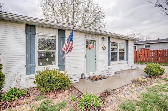 entrance to property with brick siding, fence, and a patio