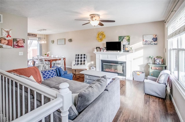 living room with wood finished floors, a ceiling fan, a glass covered fireplace, baseboards, and a chandelier