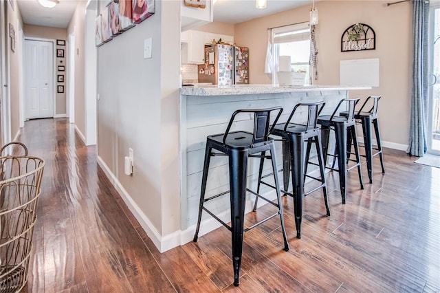 bar area with freestanding refrigerator, baseboards, dark wood-style floors, and decorative light fixtures