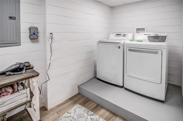washroom featuring separate washer and dryer, light wood-type flooring, wood walls, and electric panel