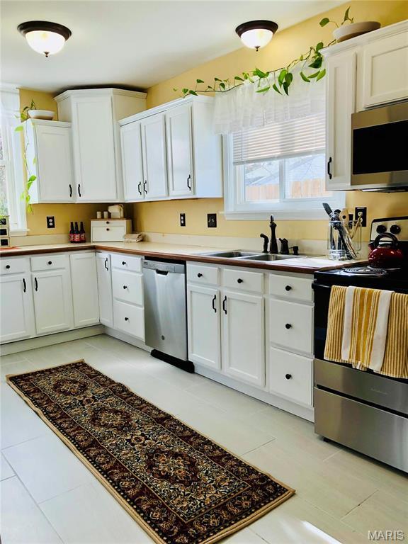 3579 Boswell, St John, MO 63114 - kitchen featuring stainless steel appliances, a sink, white cabinets, light tile patterned floors, and light countertops