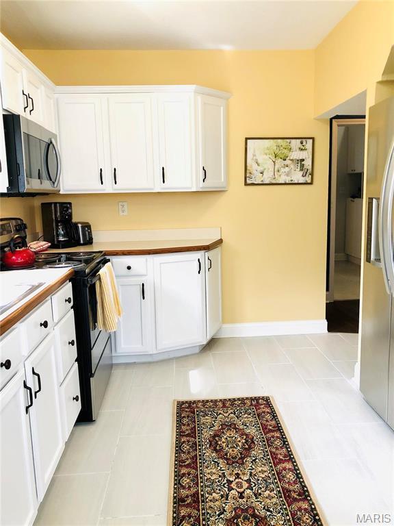 3579 Boswell, St John, MO 63114 - kitchen with stainless steel appliances, white cabinets, light countertops, light tile patterned floors, and baseboards