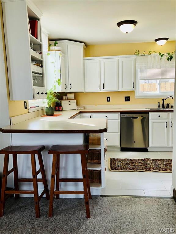 3579 Boswell, St John, MO 63114 - kitchen featuring dishwasher, a sink, white cabinetry, a breakfast bar, and a peninsula