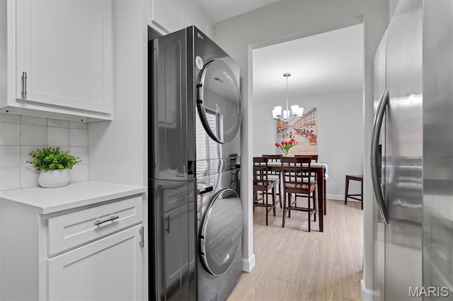 9003 Cardinal Ter, Saint Louis, MO 63144 - laundry area with stacked washer / dryer, light wood-style floors, a chandelier, baseboards, and cabinet space