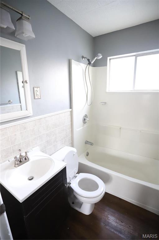 3670 E Edgar Ave, Saint Louis, MO 63121 - full bathroom with washtub / shower combination, vanity, tile walls, wood finished floors, and wainscoting