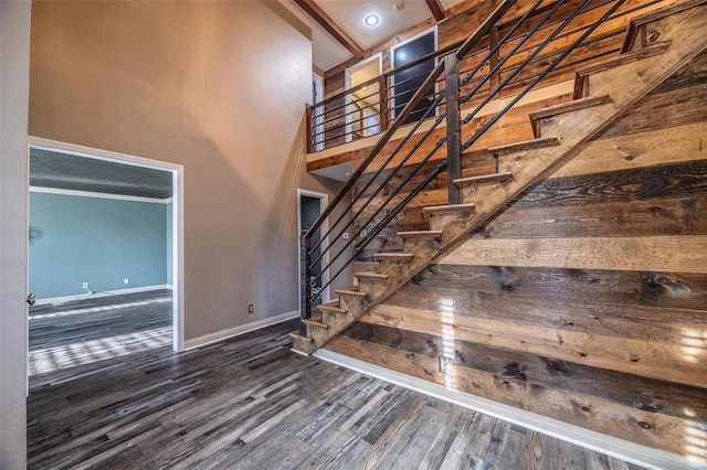 staircase with baseboards, wood finished floors, and a towering ceiling