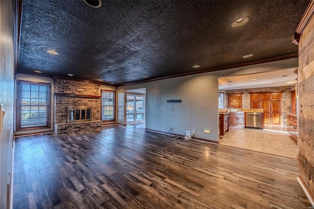 unfurnished living room with a fireplace, hardwood / wood-style flooring, healthy amount of natural light, a textured ceiling, and crown molding