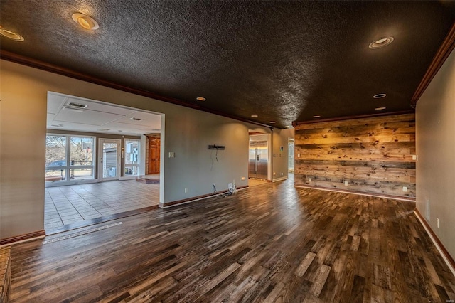 spare room featuring wood finished floors, crown molding, baseboards, wood walls, and a textured ceiling