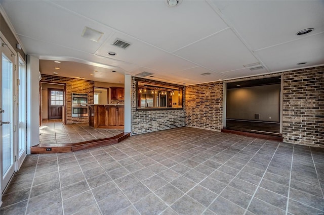 unfurnished living room featuring brick wall and tile patterned flooring