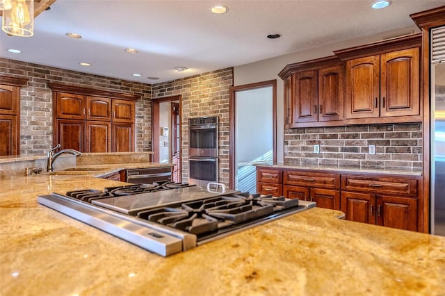 kitchen with stainless steel appliances, recessed lighting, a sink, light stone countertops, and brick wall