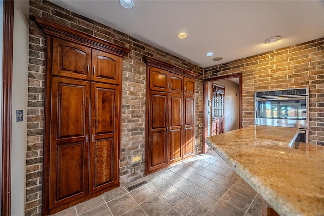 kitchen featuring brick wall, light stone countertops, recessed lighting, and tile patterned floors