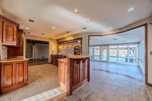 kitchen featuring brown cabinetry, a peninsula, light stone counters, and recessed lighting