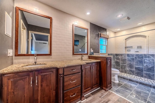 bathroom featuring tile walls, a tile shower, double vanity, a textured ceiling, and toilet