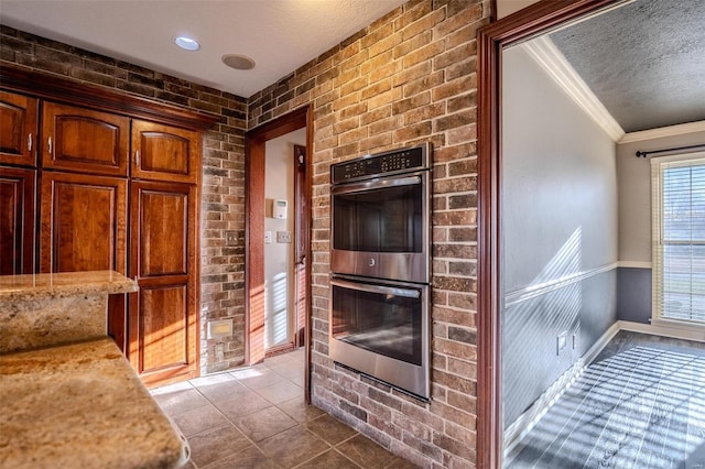 kitchen featuring double oven, a textured ceiling, ornamental molding, brick wall, and tile patterned flooring