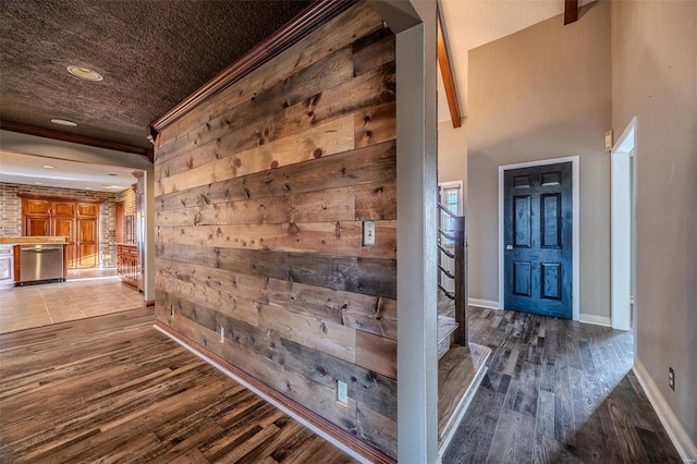 hall featuring wood finished floors, wooden walls, stairs, baseboards, and ornamental molding