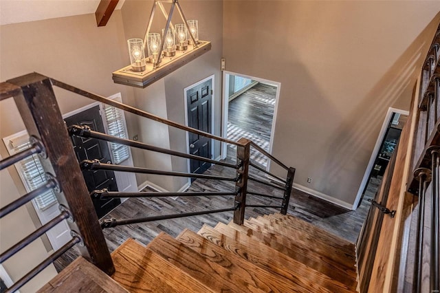 stairway with wood finished floors, a high ceiling, baseboards, and a chandelier