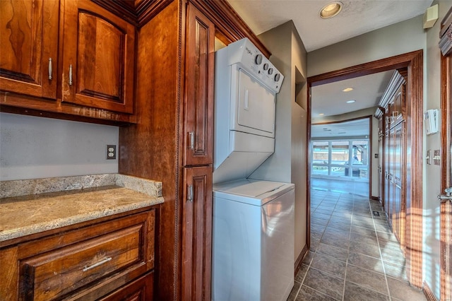 washroom with stacked washer / drying machine and dark tile patterned floors
