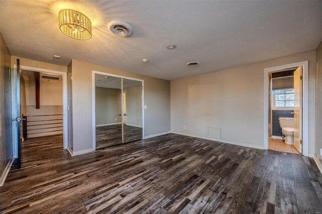 unfurnished bedroom with dark wood-style flooring, a closet, baseboards, a textured ceiling, and ensuite bath