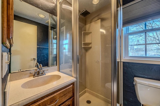 full bath featuring a stall shower, healthy amount of natural light, toilet, vanity, and a textured ceiling