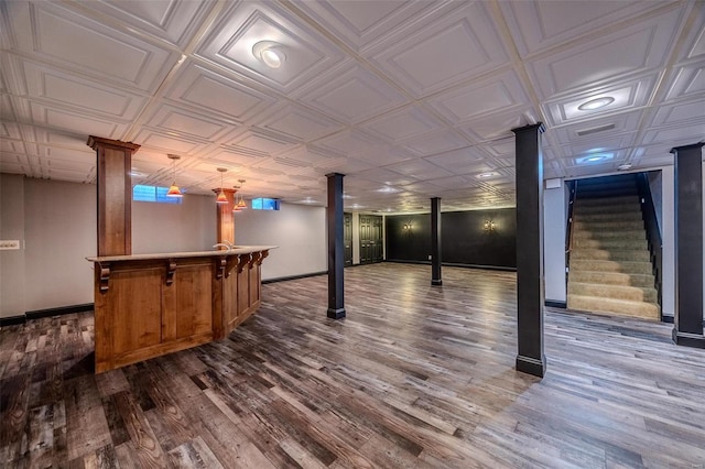 finished basement featuring bar, stairway, dark wood-style flooring, baseboards, and an ornate ceiling