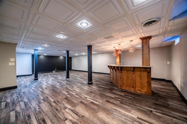 finished basement featuring a dry bar, dark wood-type flooring, baseboards, and an ornate ceiling