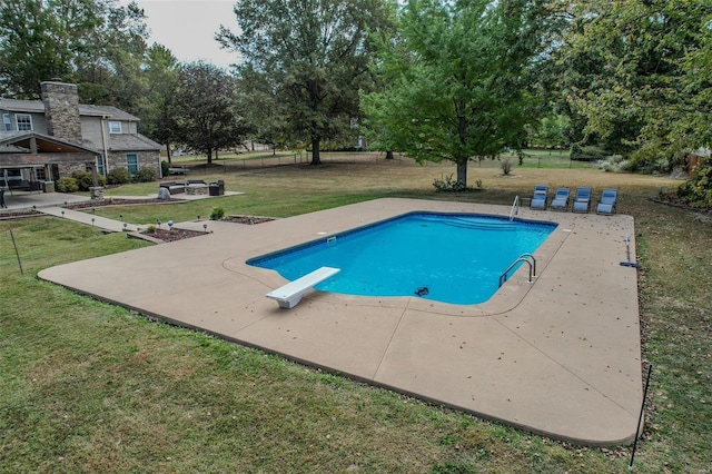outdoor pool with a patio area, a yard, and a diving board