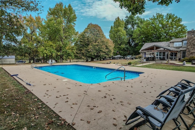 outdoor pool with a patio, a yard, and a diving board