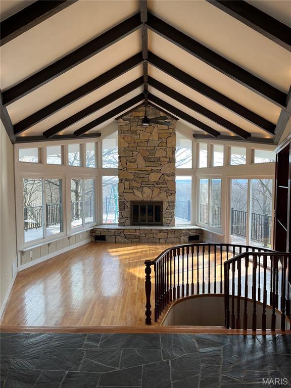 unfurnished living room with healthy amount of natural light, a stone fireplace, wood finished floors, and baseboards