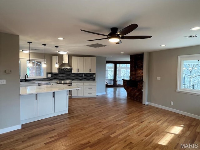 kitchen featuring wall chimney exhaust hood, stove, baseboards, ceiling fan, and backsplash