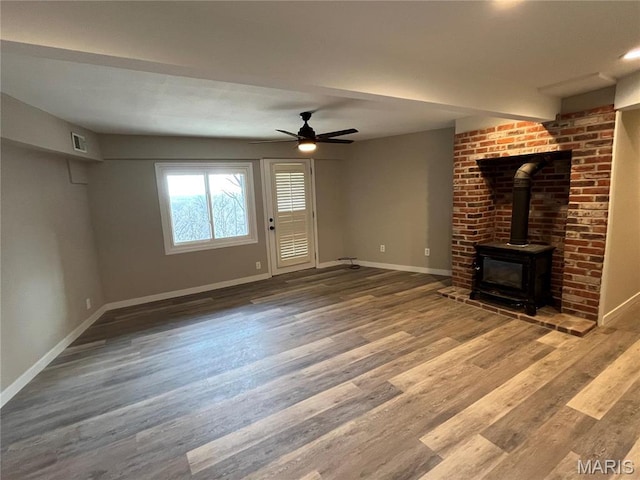 unfurnished living room with a wood stove, baseboards, wood finished floors, and a ceiling fan