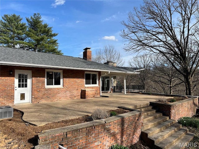 back of property featuring brick siding, a chimney, central air condition unit, and roof with shingles