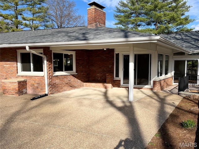 back of house featuring brick siding, roof with shingles, a chimney, and a patio