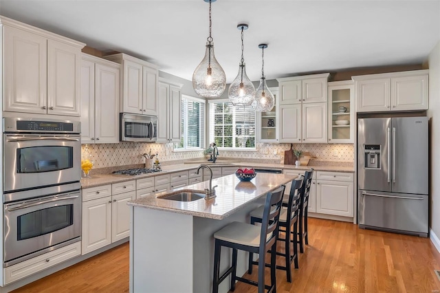 kitchen with appliances with stainless steel finishes, a sink, white cabinetry, glass insert cabinets, and light wood-type flooring