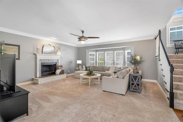 carpeted living room with stairs, a ceiling fan, ornamental molding, baseboards, and a tiled fireplace