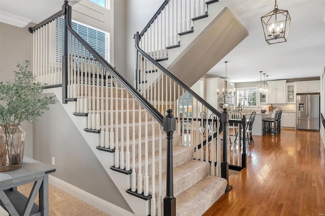 staircase with a chandelier, wood finished floors, and baseboards