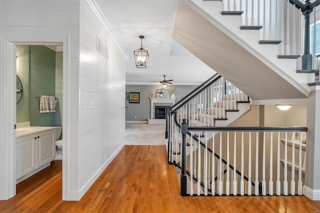 stairway featuring baseboards, a ceiling fan, ornamental molding, and wood finished floors