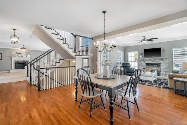 dining space with a stone fireplace, ceiling fan, ornamental molding, and wood finished floors