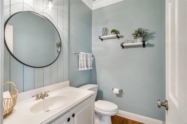 bathroom featuring toilet, ornamental molding, vanity, wood finished floors, and baseboards
