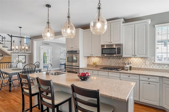kitchen featuring appliances with stainless steel finishes, a sink, a center island with sink, tasteful backsplash, and white cabinets