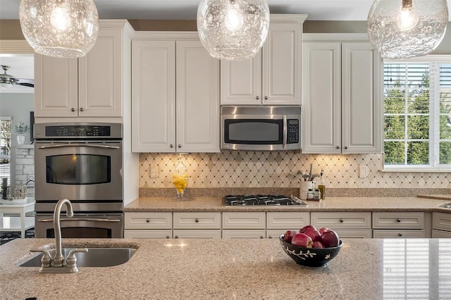 kitchen with stainless steel appliances, a sink, white cabinetry, light stone counters, and backsplash