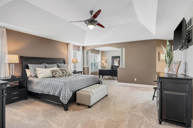 bedroom with light colored carpet, arched walkways, a raised ceiling, baseboards, and decorative columns