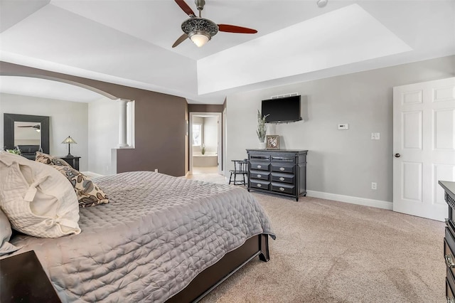 bedroom with a tray ceiling, arched walkways, light carpet, decorative columns, and baseboards