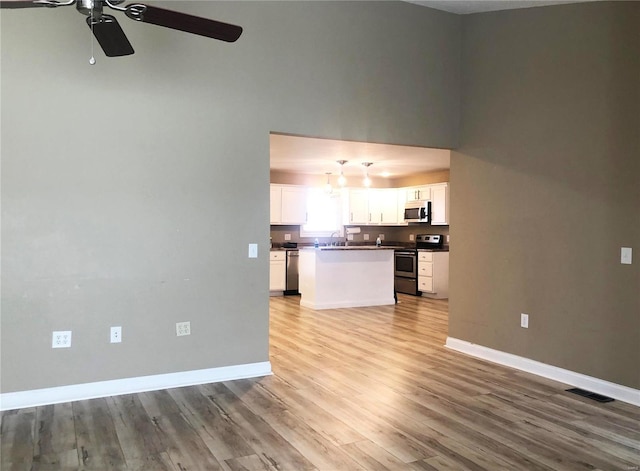 unfurnished living room featuring ceiling fan, light wood-style floors, baseboards, and a sink