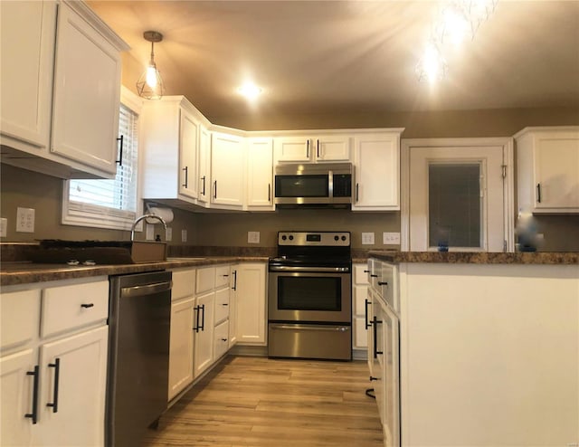 kitchen featuring appliances with stainless steel finishes, white cabinets, light wood-style floors, and dark countertops