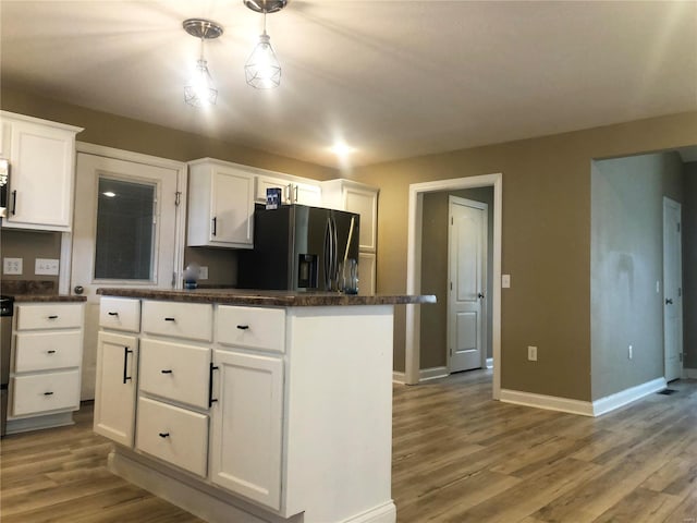 kitchen with stainless steel fridge, dark countertops, white cabinets, and wood finished floors