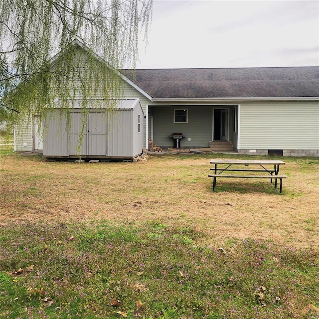 back of house featuring a lawn, entry steps, a shingled roof, and an outdoor structure